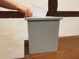 Symbolbild Wahlurne in die ein Zettel geworfen wird.